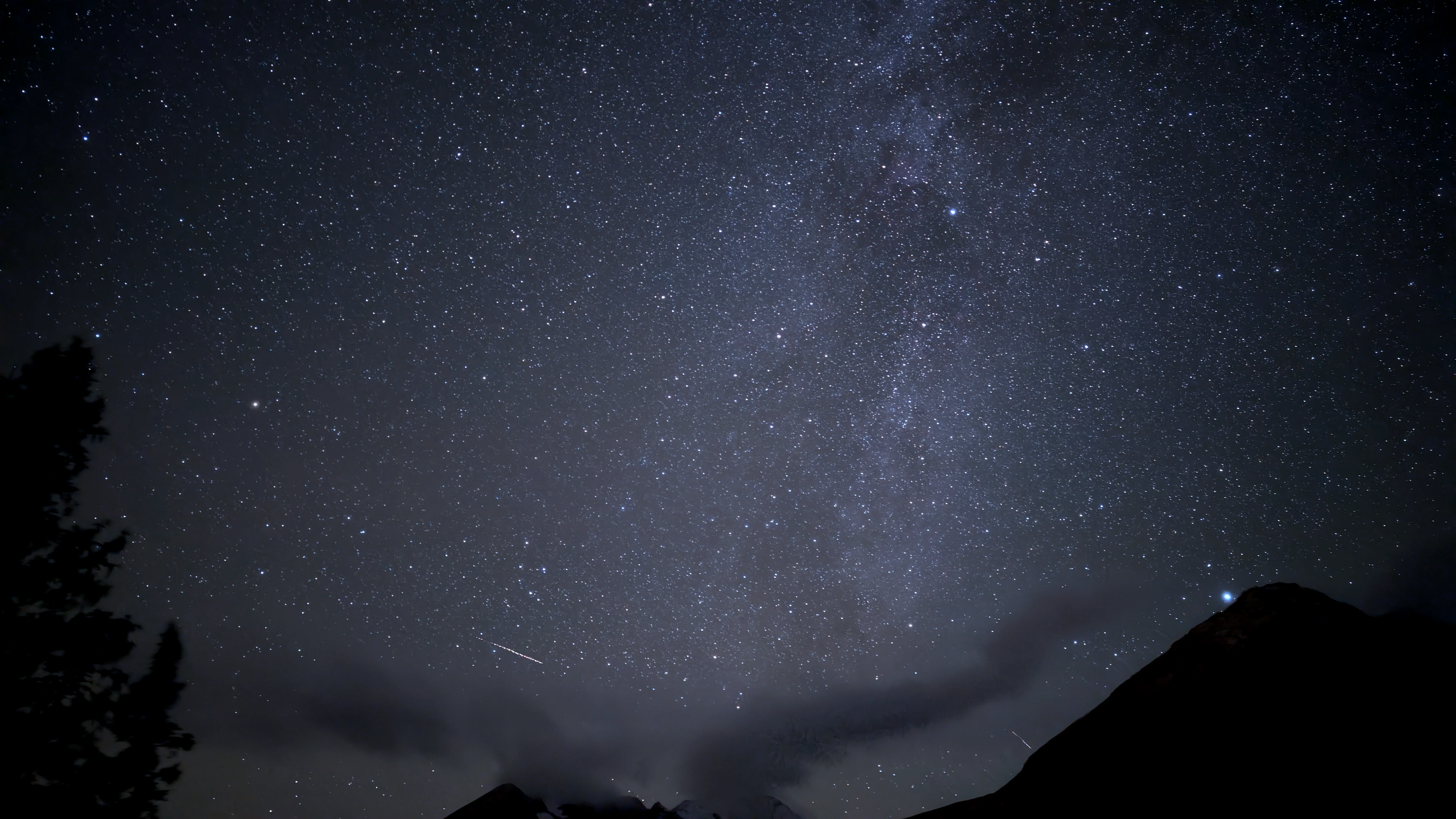 Sternenhimmel bei Nacht mit sichtbarem Band der Milchstraße und einer Sternschnuppe über dunkler Gebirgssilhouette