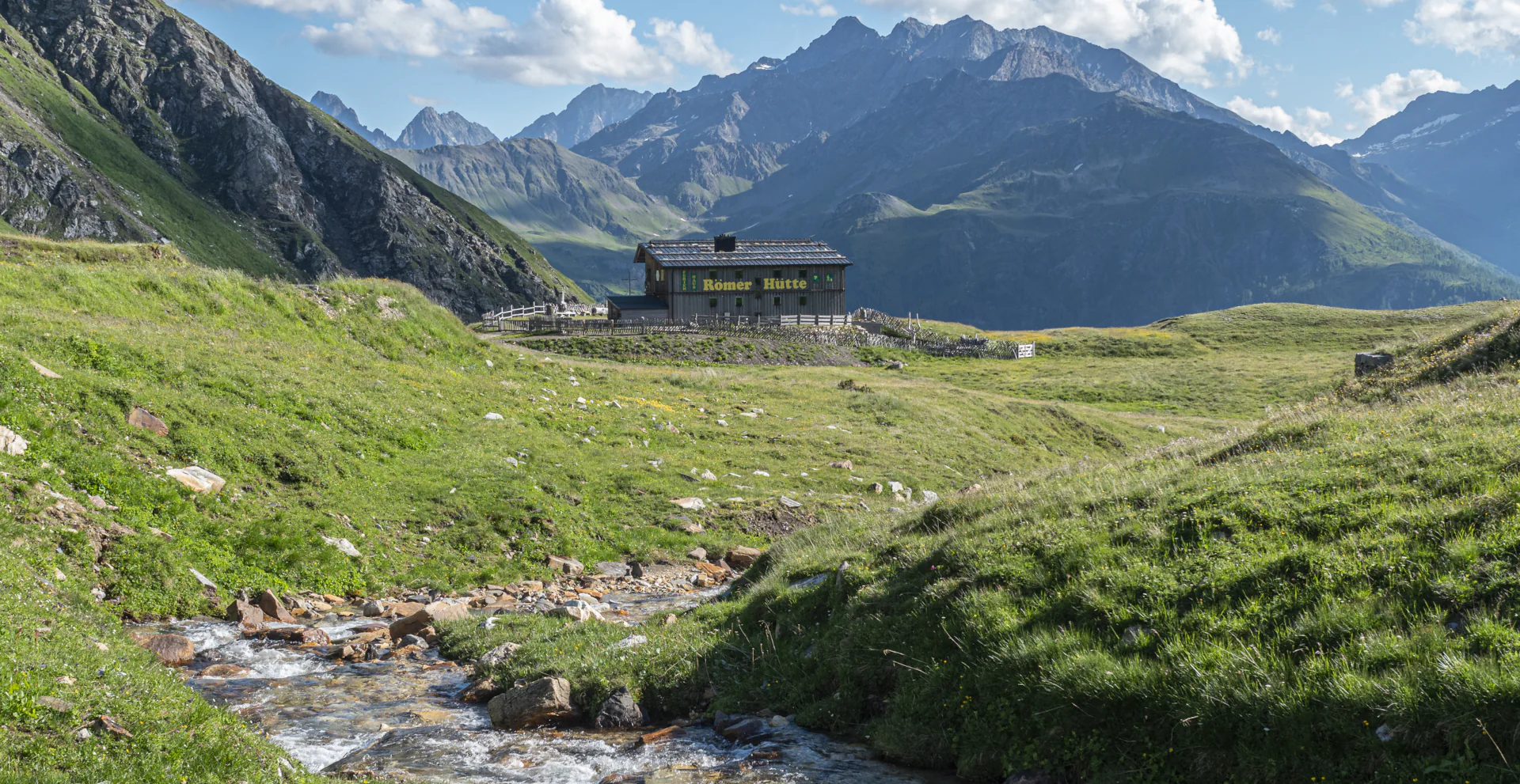 Tauernbach mit dem Ferienhaus Römerhütte im Hintergrund, dahinter Berge der Schobergruppe zu sehen